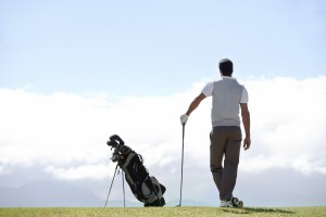 Mature golfer standing and admiring the view on the golf course alongside his clubs - rear view