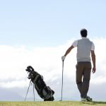 Mature golfer standing and admiring the view on the golf course alongside his clubs - rear view